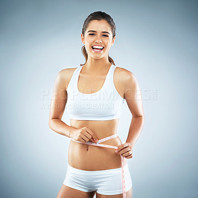 Buy stock photo Studio portrait of an attractive young woman measuring her waist against a grey background