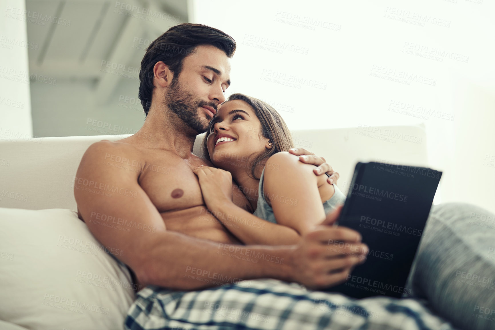 Buy stock photo Cropped shot of an affectionate young couple relaxing on the sofa with a tablet