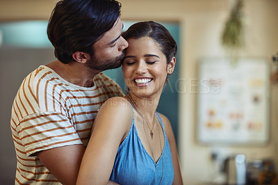 Buy stock photo Shot of an affectionate young couple kissing in their kitchen at home