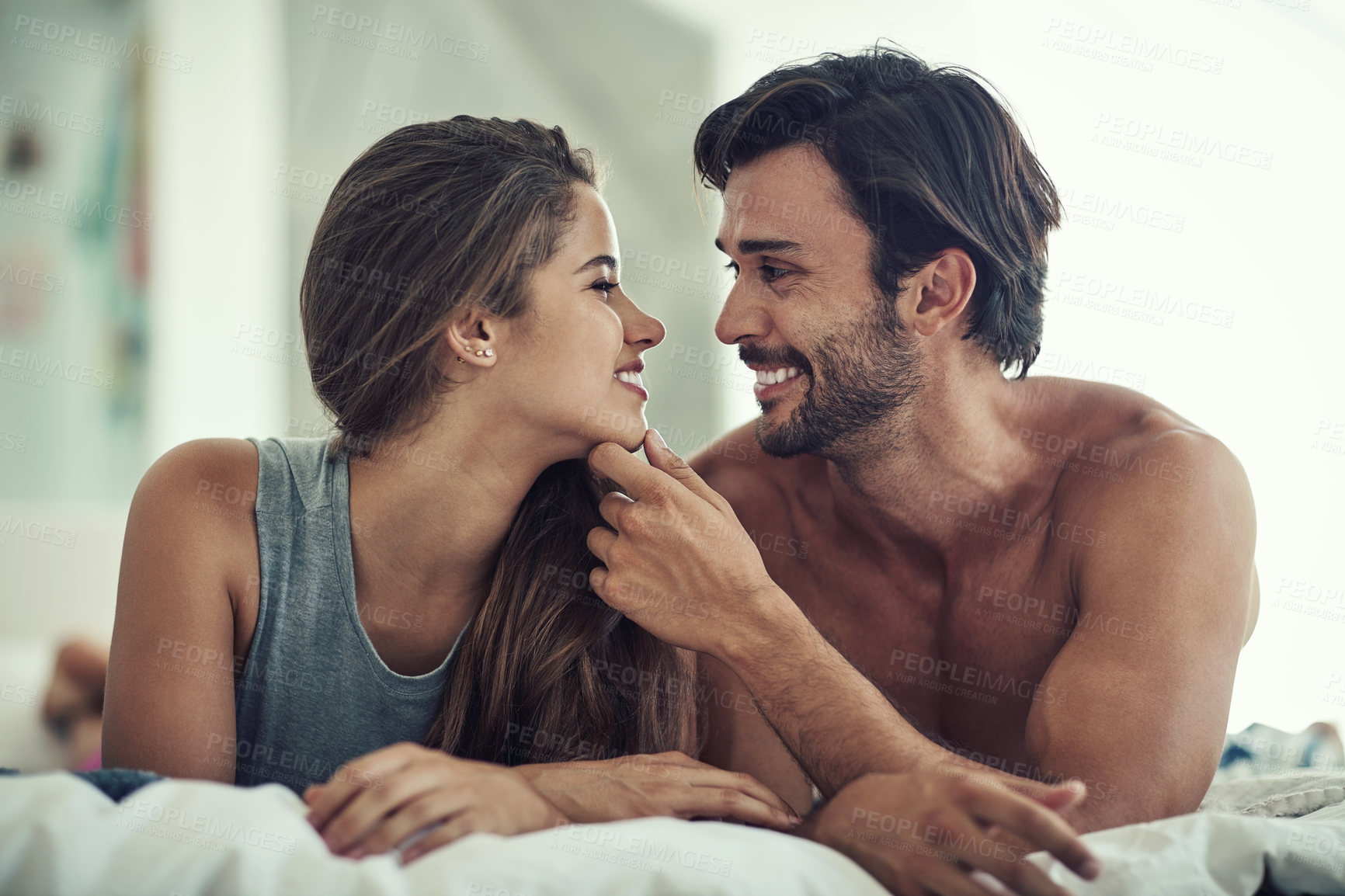 Buy stock photo Couple, happy and relax for love in bedroom with hand on chin for marriage commitment, romance and bonding. Smile, woman and man with support of trust, healthy relationship and care together at house