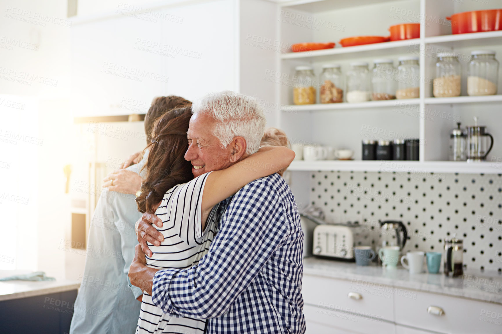 Buy stock photo Shot of a loving family greeting each other with hugs in the kitchen at home