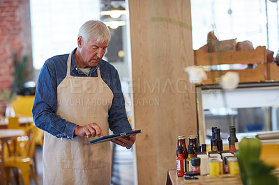 Buy stock photo Shot of a happy senior business owner using a tablet in his coffee shop