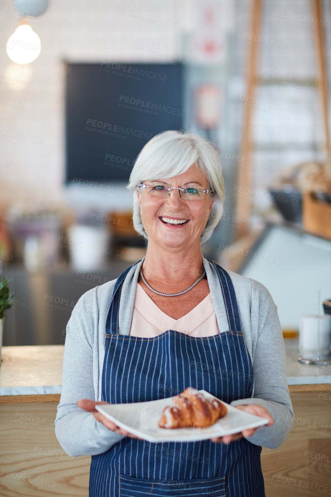 Buy stock photo Portrait of a happy senior business owner holding a plate with a pastry on it in her coffee shop