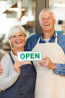 Buy stock photo Portrait of two happy senior business owners holding an open sign while standing inside their coffee shop