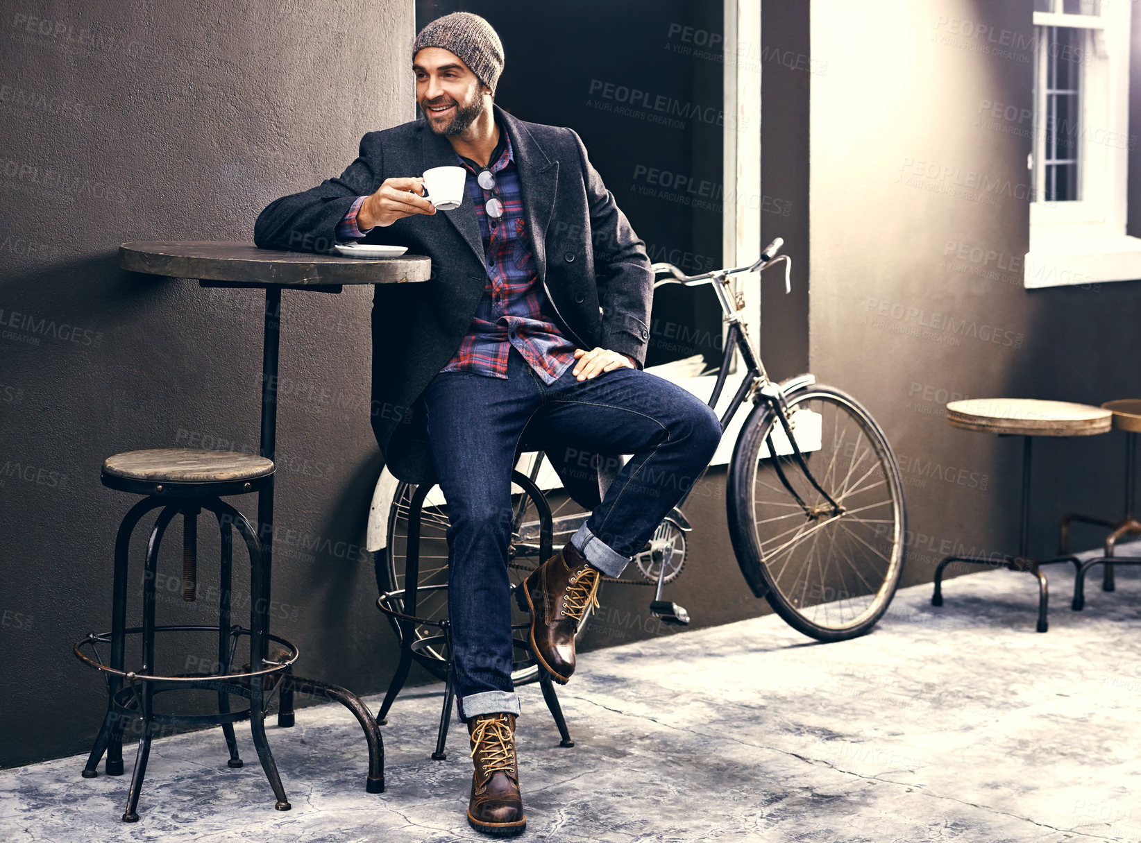Buy stock photo Shot of a handsome young man enjoying a cup of coffee at a cafe in the city while his bike stands next to him