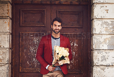 Buy stock photo Shot of a handsome young man standing outside a door with a bunch of flowers looking smart and happy