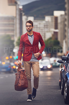 Buy stock photo Shot of a handsome young man  walking in the road while carrying his bag looking determined