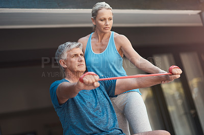 Buy stock photo Shot of a mature man stretching his arm muscles with an elastic band while being assisted by a woman