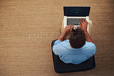 Buy stock photo High angle shot of a young man using his laptop while sitting at home