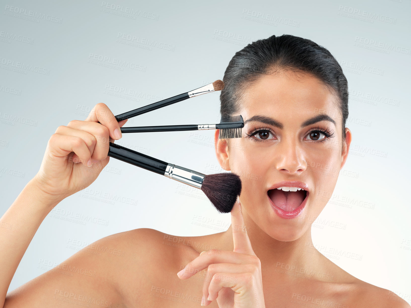 Buy stock photo Studio shot of a beautiful young woman holding makeup brushes against a gray background