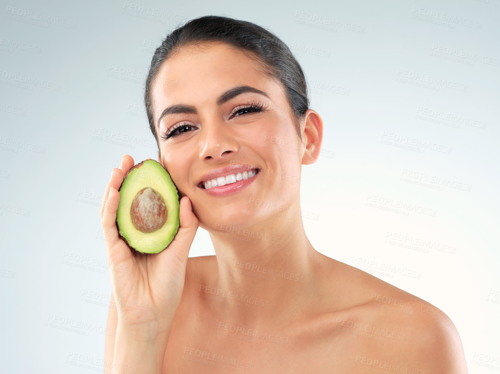 Buy stock photo Studio portrait of a beautiful young woman covering her eye with an avocado against a gray background