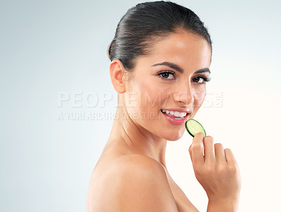 Buy stock photo Studio portrait of a beautiful young woman eating a slice of cucumber against a gray background