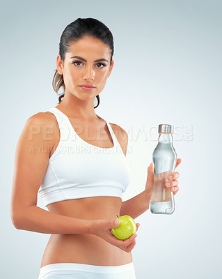 Buy stock photo Studio shot of a fit young woman holding a bottle of water and an apple against a gray background