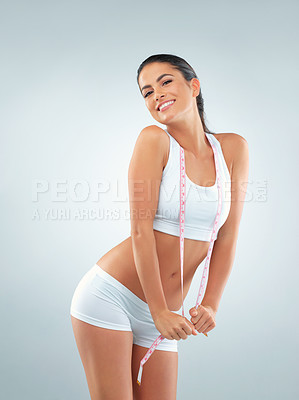 Buy stock photo Studio shot of a fit young woman posing with a measuring tape against a gray background