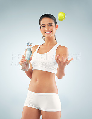 Buy stock photo Studio shot of a fit young woman holding a bottle of water and tossing an apple against a gray background