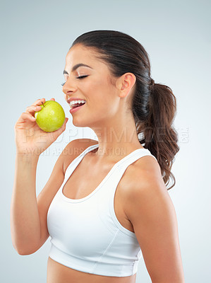 Buy stock photo Studio shot of a fit young woman eating an apple against a gray background