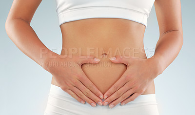 Buy stock photo Cropped studio shot of a fit young woman with her hands framing her stomach against a gray background
