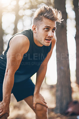 Buy stock photo Shot of a young man resting from a run outside in the forest
