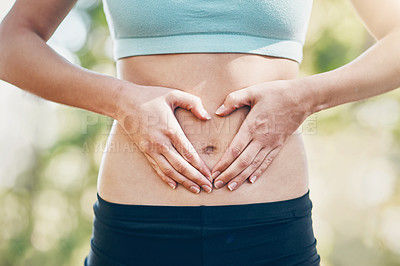 Buy stock photo Shot of a young woman making a heart shape with her hands around her belly button outdoors