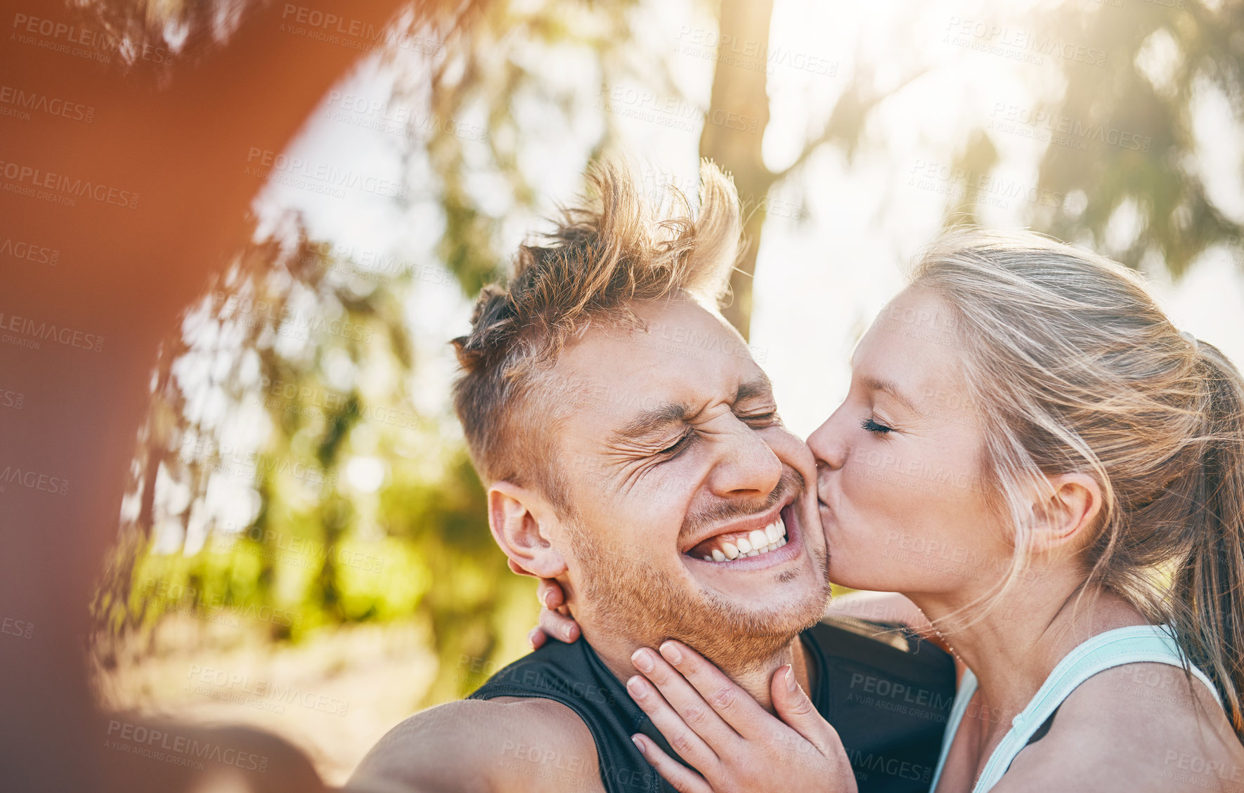 Buy stock photo Shot of a young woman kissing her boyfriend on the cheek outside