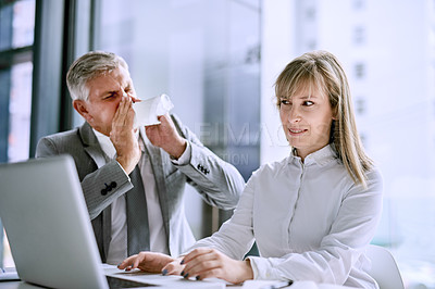 Buy stock photo Shot of a sick businessman sneezing in front of a businesswoman in the office