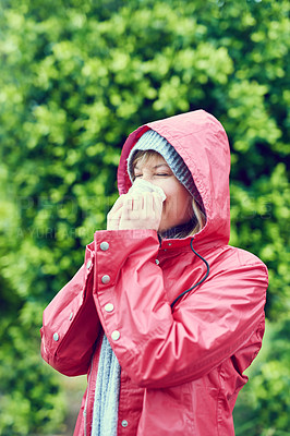 Buy stock photo Shot of a young woman blowing her nose with a tissue outdoors