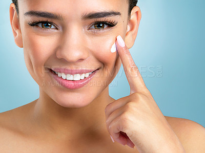 Buy stock photo Close up studio shot of a beautiful young woman applying moisturiser on her face against a blue background