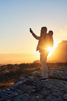 Buy stock photo Shot of a hiker standing on top of a mountain taking photos with his cellphone