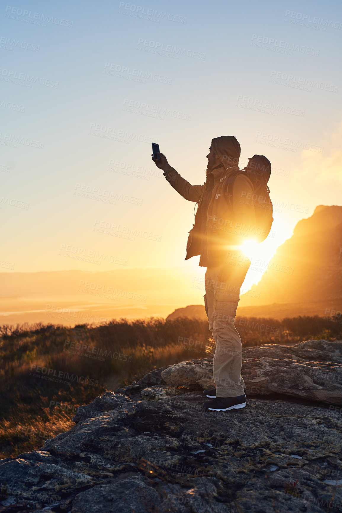 Buy stock photo Shot of a hiker standing on top of a mountain taking photos with his cellphone
