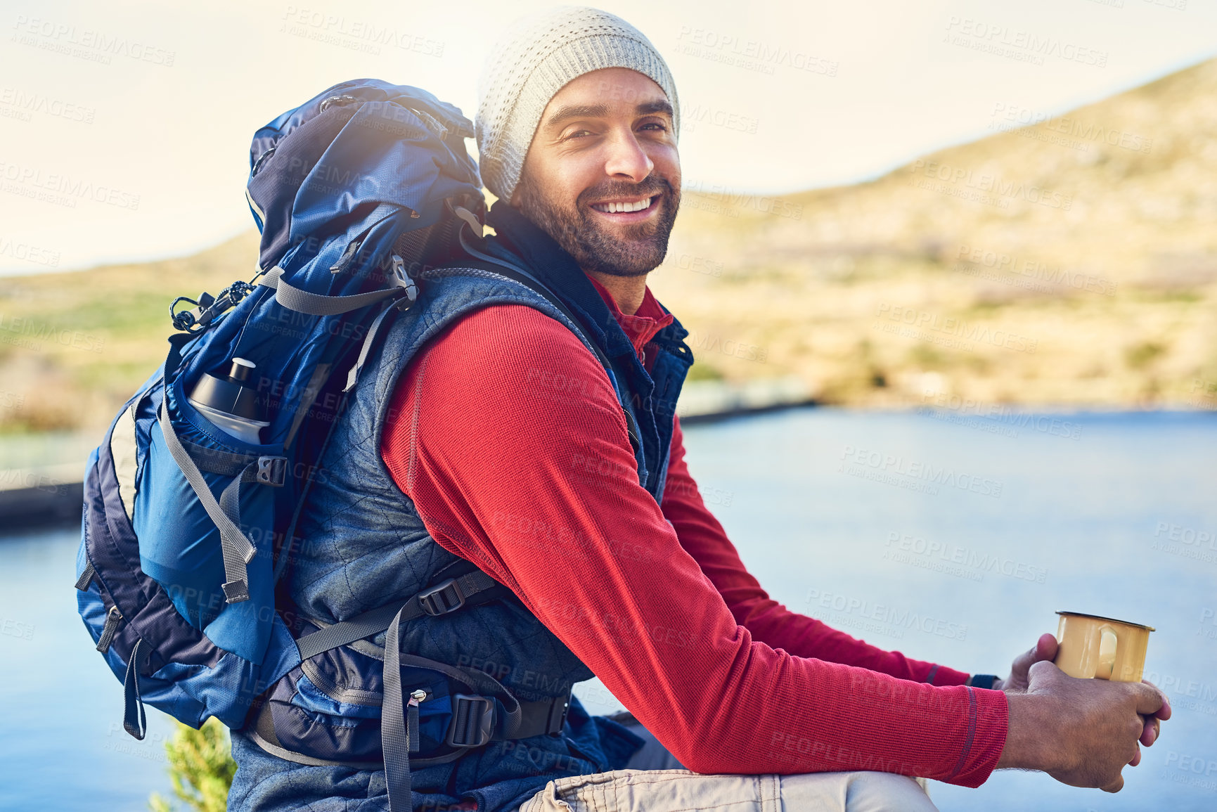 Buy stock photo Portrait of a happy hiker drinking coffee while admiring a lake view on a trail