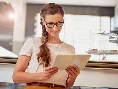 Buy stock photo Shot of happy young business owner using a tablet while standing in her coffee shop
