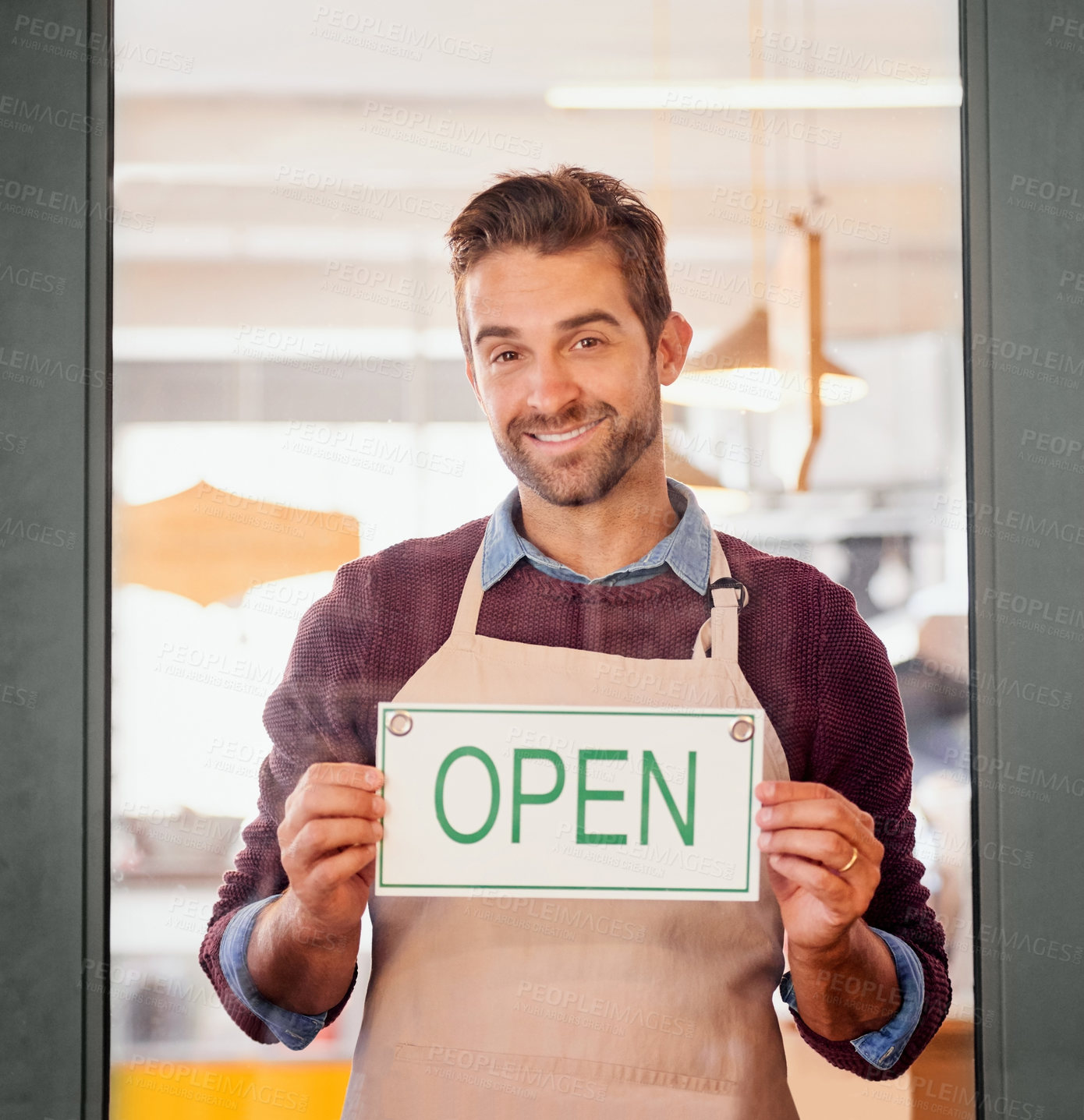 Buy stock photo Portrait of a young business owner standing in the doorway of his coffee shop with an open sign