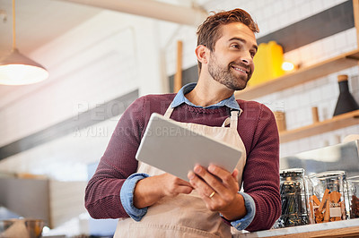 Buy stock photo Shot of happy young business owner using a tablet while standing in his coffee shop