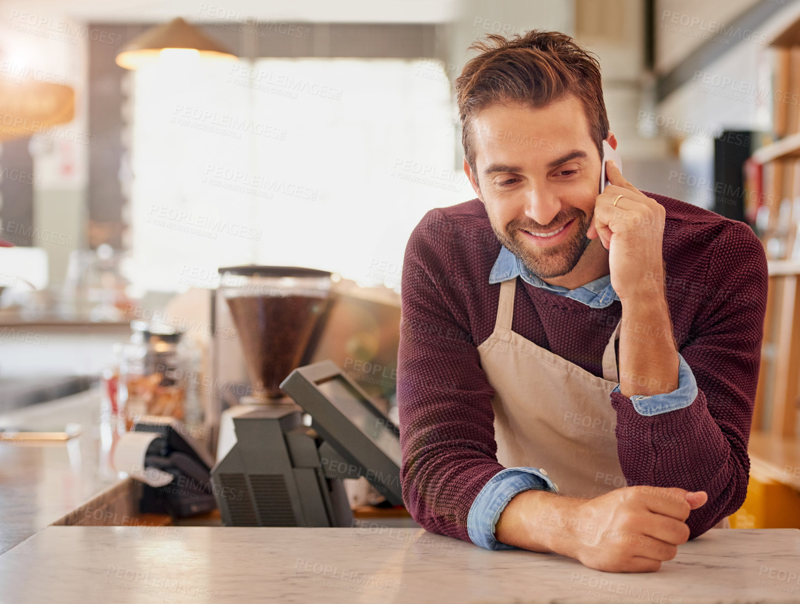 Buy stock photo Shot of a happy business owner using his smartphone while leaning on the counter in his coffee shop