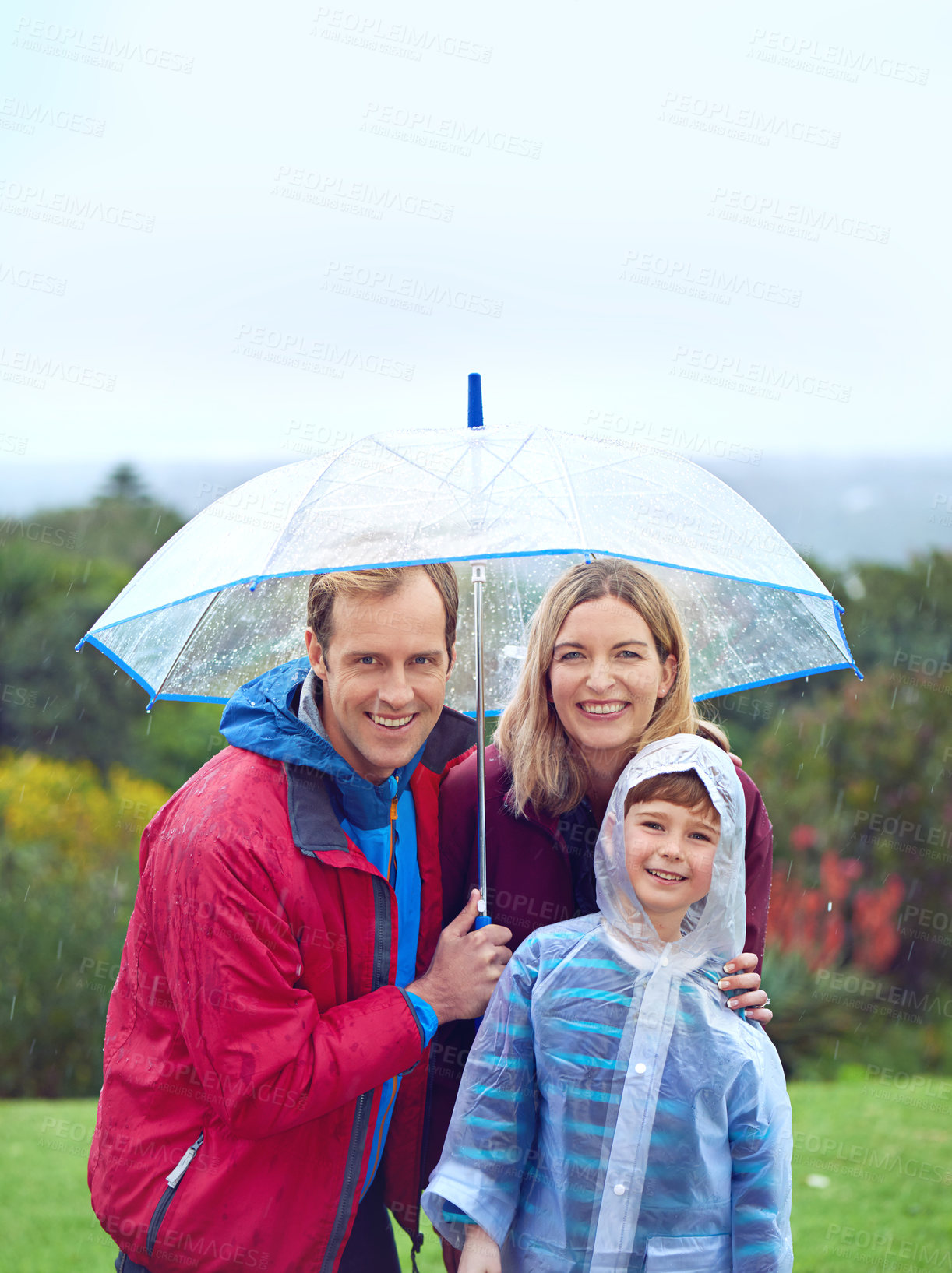 Buy stock photo Rain, outdoor and a happy family with umbrella for a portrait in nature for fun, happiness and quality time. Man, woman and boy child together for water drops and freedom while playing at a park