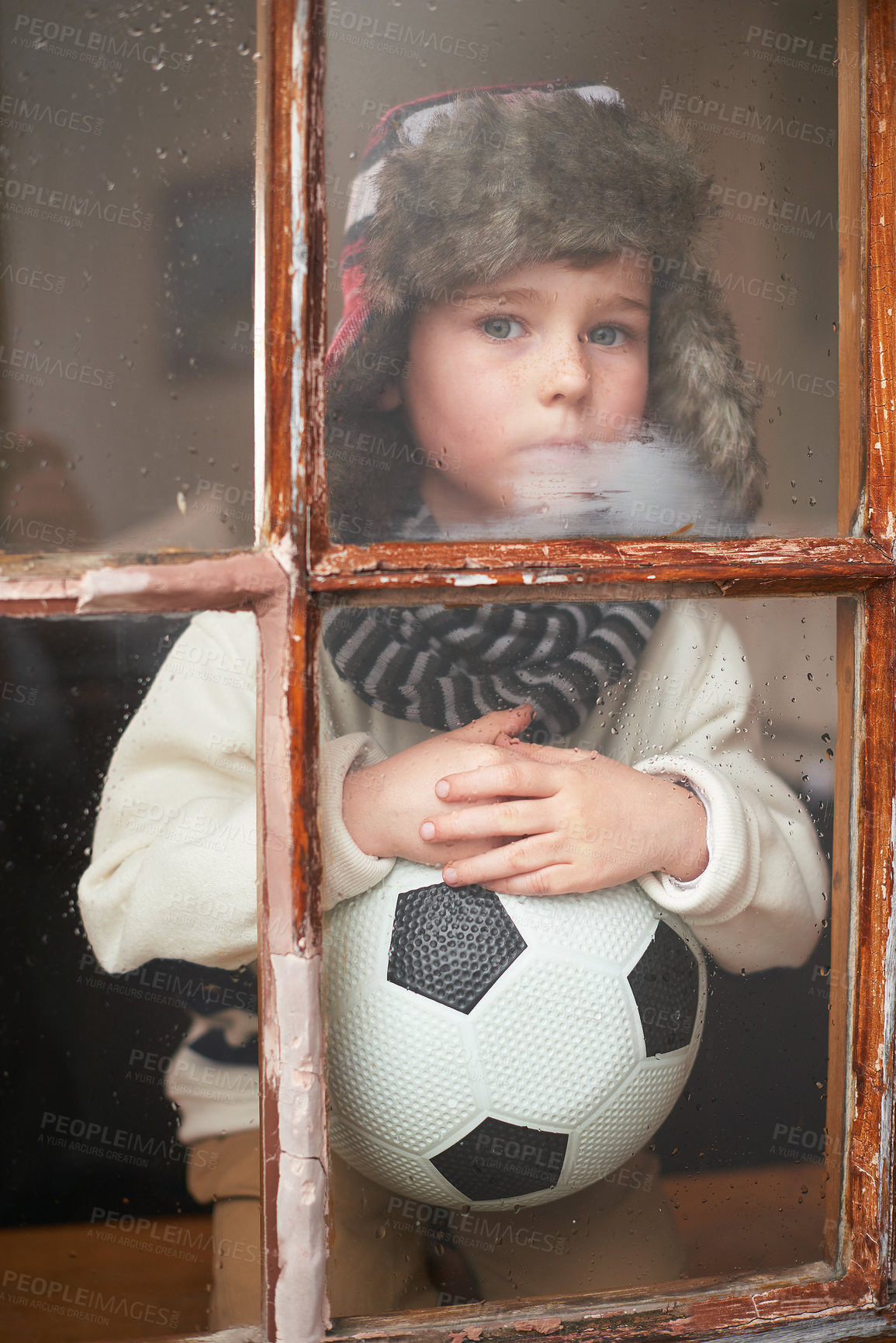 Buy stock photo Boy, sad and ball by window for soccer in house during winter with rain for sports or fun game. Child, anxiety and thinking by glass frame for bullying, lonely and scared as orphan without friends