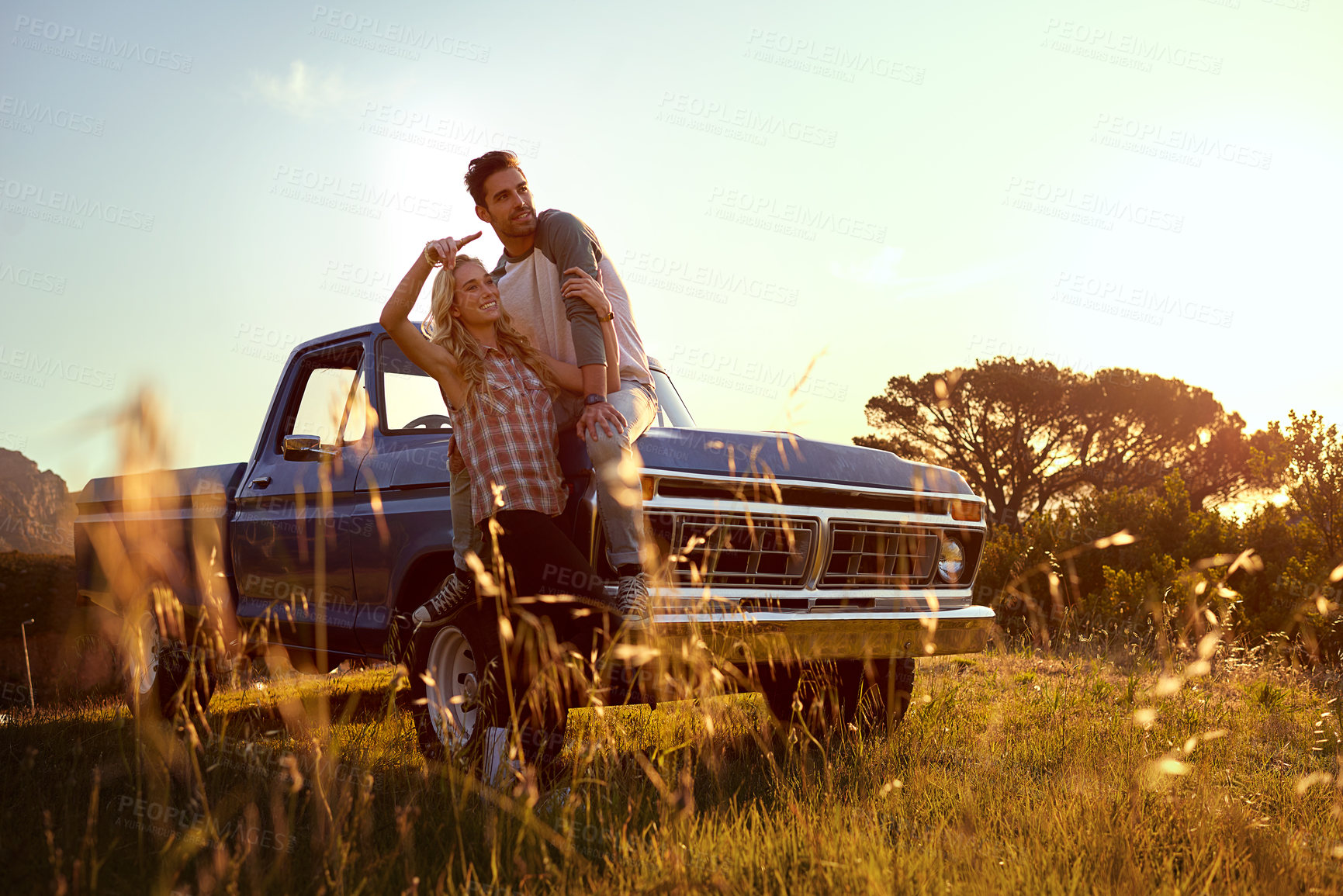 Buy stock photo Couple, relax and car with sunset for road trip, vacation or holiday together in countryside. Man, woman or lovers with smile for adventure, travel or sightseeing on vehicle or grass field in nature