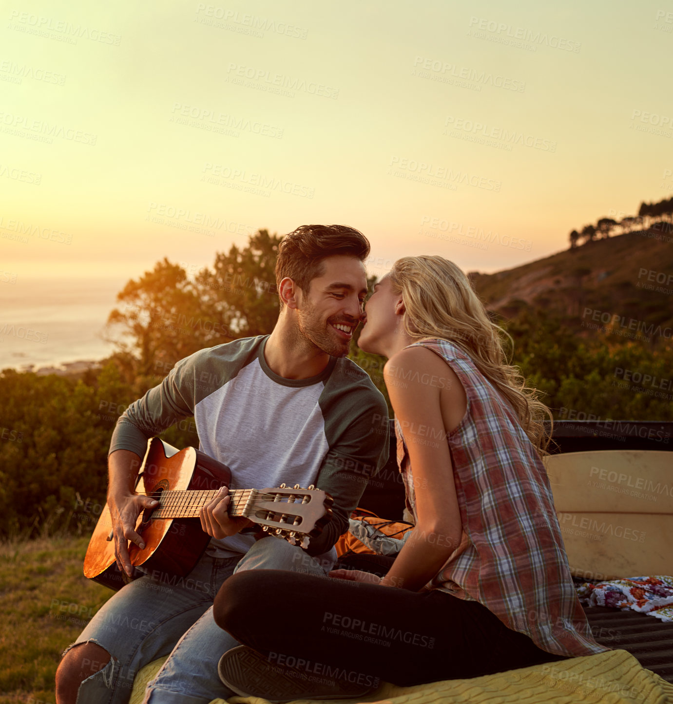 Buy stock photo Guitar, happy and couple playing music in nature by sunset on date for romantic getaway road trip. Kiss, outdoor and man serenading woman with string instrument in field for vacation or holiday.