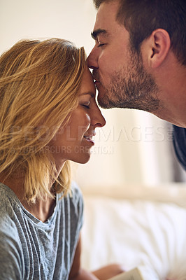 Buy stock photo Close up shot of a handsome man kissing his attractive girlfriend on the forehead at home at home