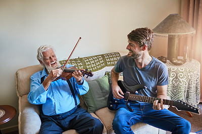 Buy stock photo Shot of a young man playing the electric guitar while his elderly grandfather plays the violin on the couch