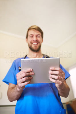Buy stock photo Shot of a happy young doctor using his tablet in his office