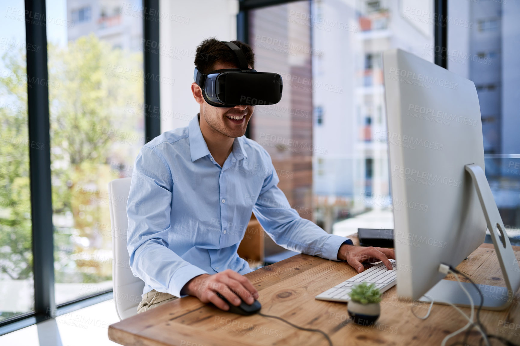 Buy stock photo Shot of a happy young businessman wearing a virtual reality headset while working at his desk in the office