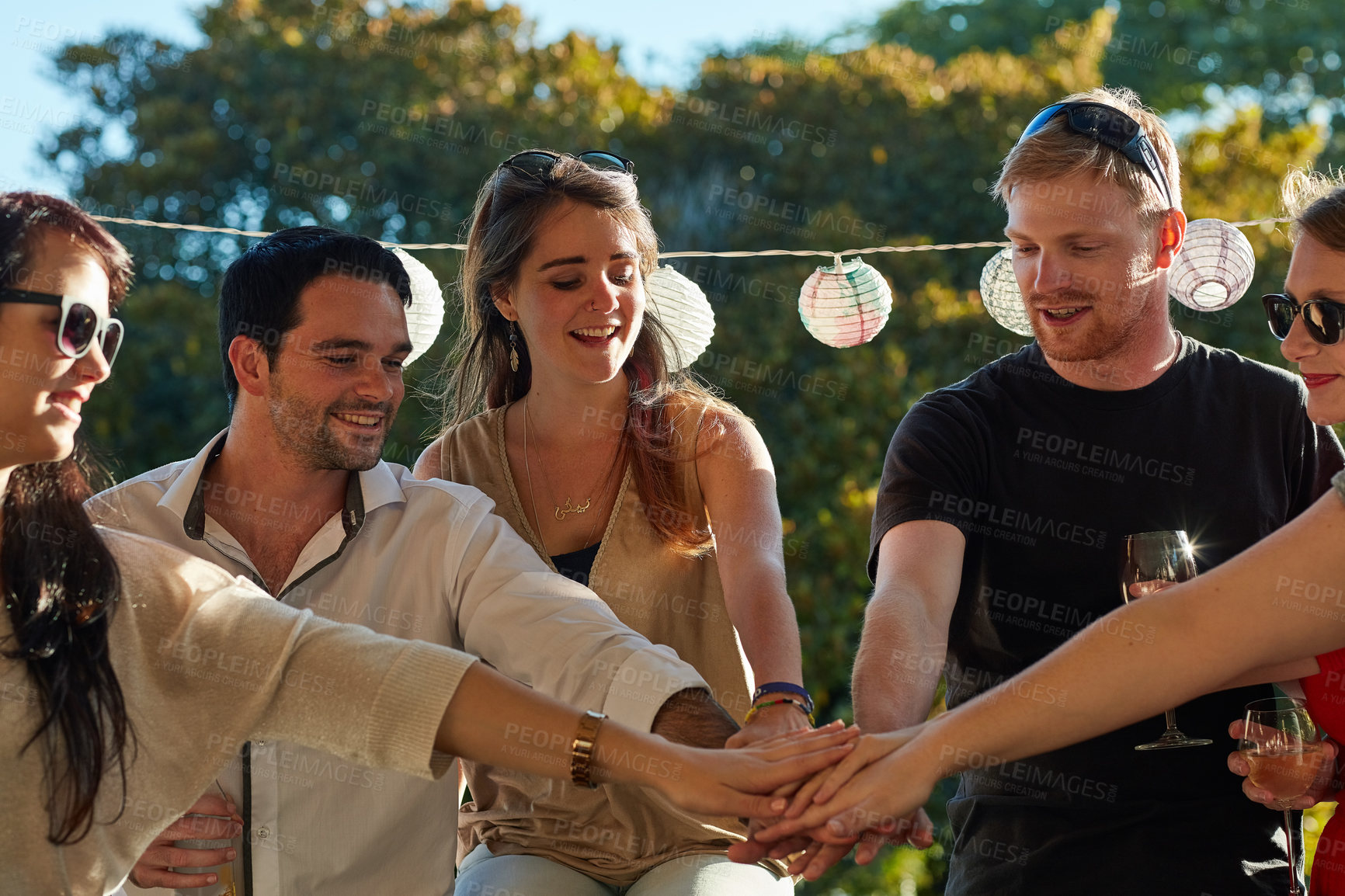 Buy stock photo Shot of a group of happy young friends putting their hands in a pile at an outdoor party