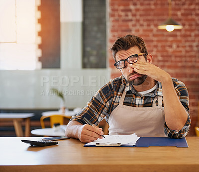 Buy stock photo Shot of an exhausted young business owner doing admin at a table in his coffee shop