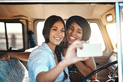 Buy stock photo Shot of two happy friends taking selfies with a mobile phone on a roadtrip