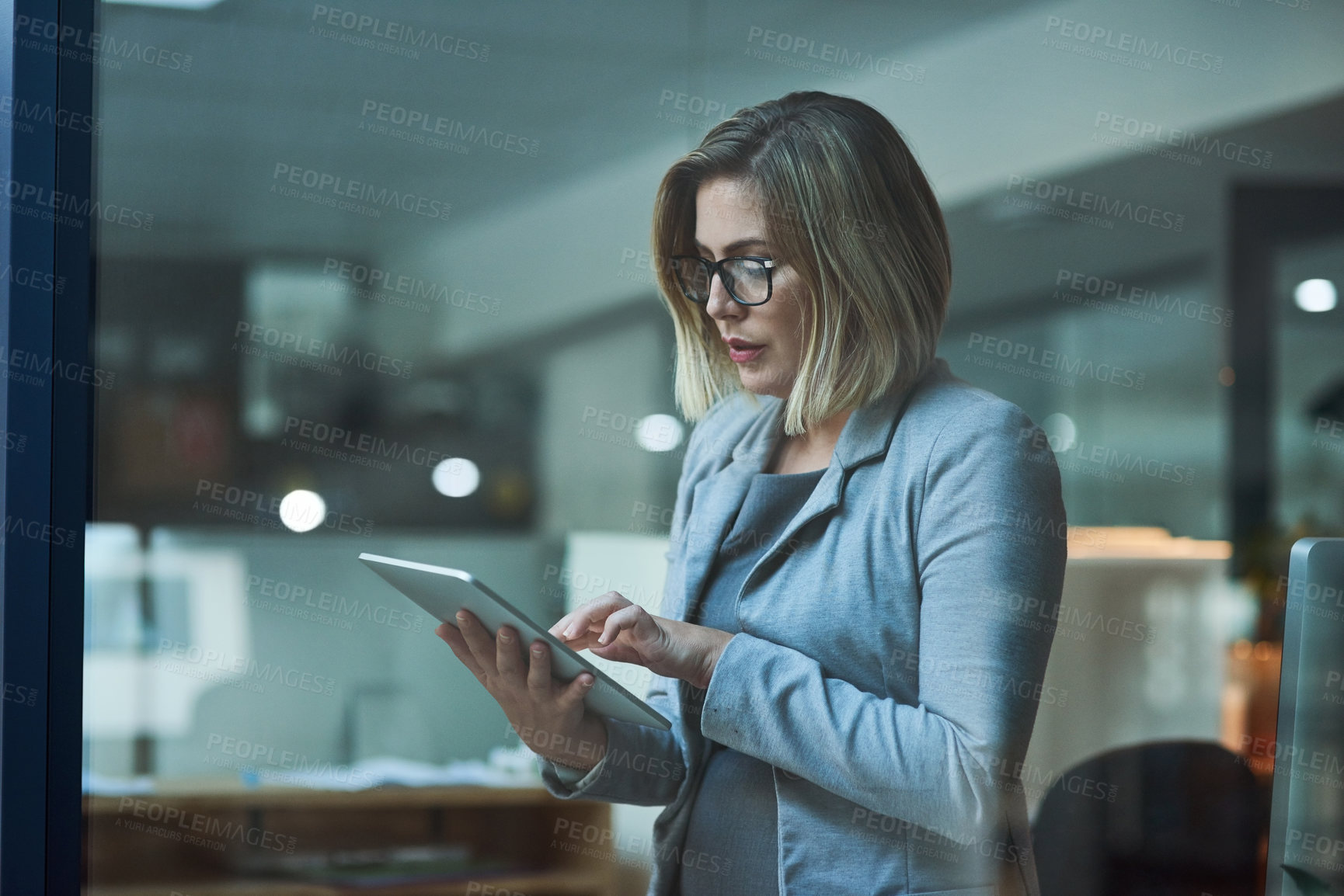 Buy stock photo Cropped shot of a businesswoman working on a digital tablet in her office late into the night
