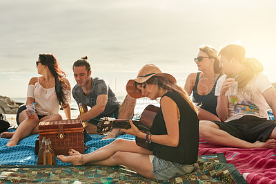 Buy stock photo Shot of a group of happy young friends enjoying a picnic on the beach together