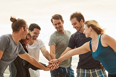 Buy stock photo Shot of a group of happy young friends putting their hands in a pile on the beach