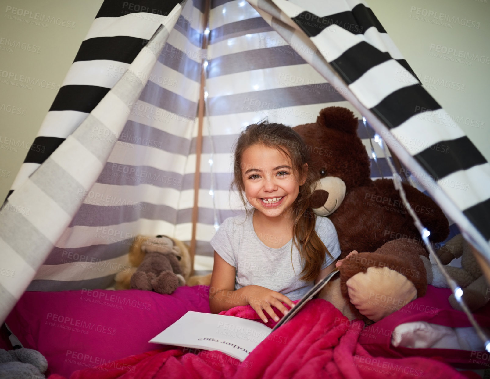 Buy stock photo Portrait of a little girl reading a book with her teddybear in a tent at home