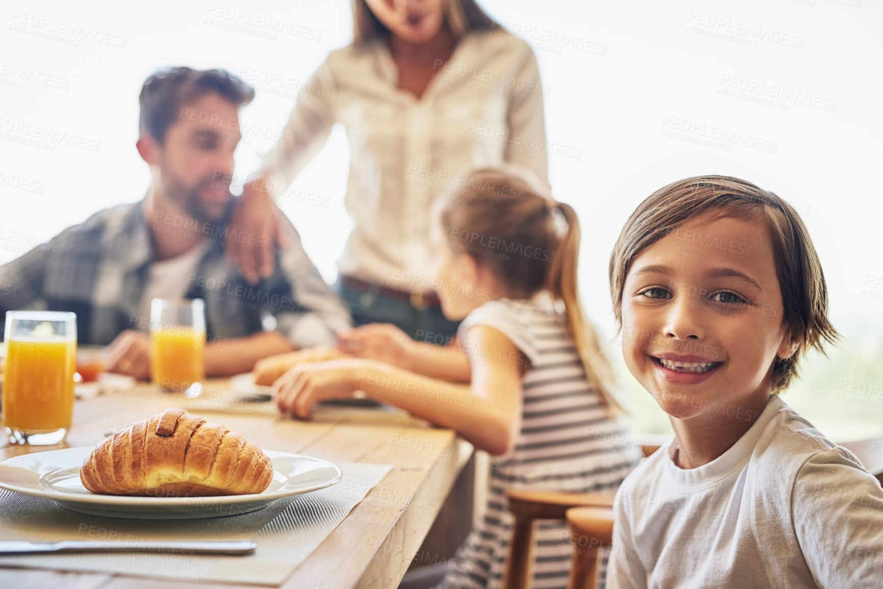 Buy stock photo Portrait of a little boy having breakfast with his family in the background